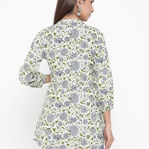 May include: A white tunic top with a floral print in shades of green and blue. The top has a V-neckline and long sleeves with a gathered cuff.