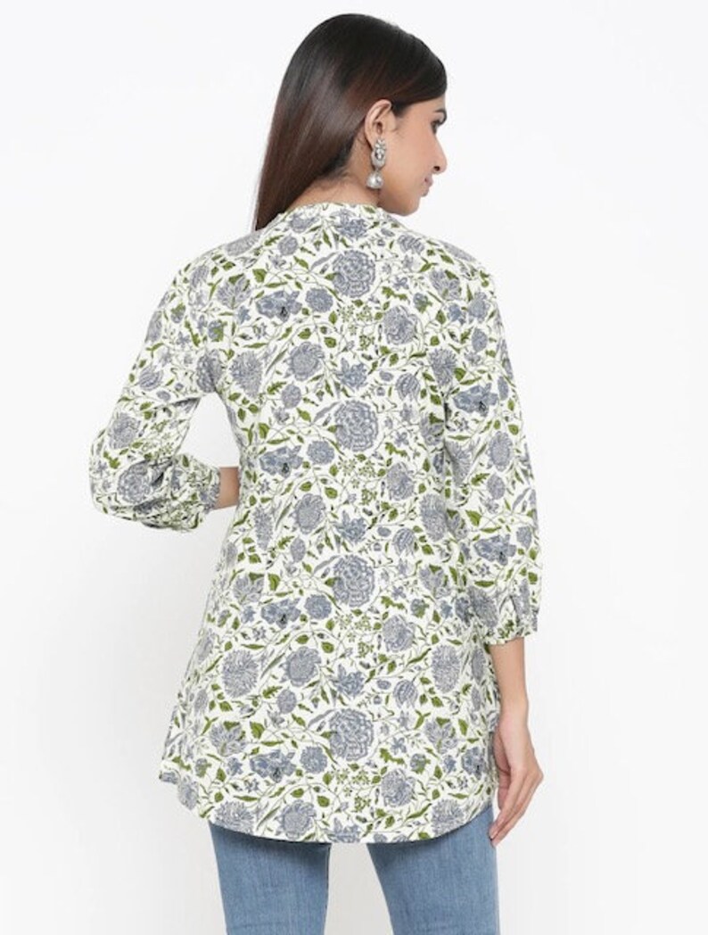 May include: A white tunic top with a floral print in shades of green and blue. The top has a V-neckline and long sleeves with a gathered cuff.
