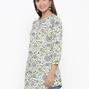May include: A white long-sleeved tunic top with a floral print in shades of blue and green. The top has a V-neckline and a button closure at the neckline.
