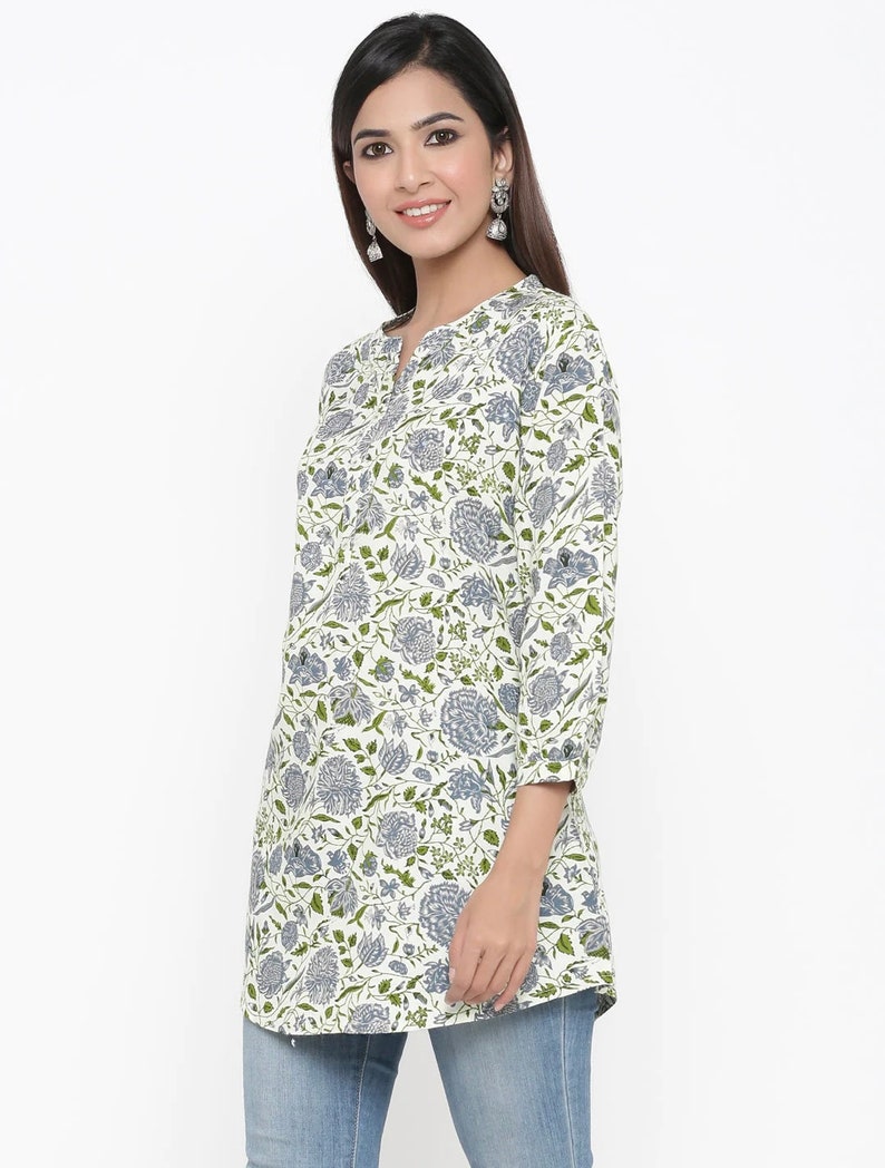 May include: A white long-sleeved tunic top with a floral print in shades of blue and green. The top has a V-neckline and a button closure at the neckline.
