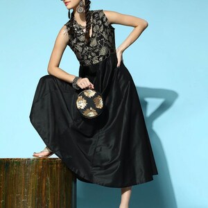 May include: A black sleeveless dress with a gold floral pattern on the bodice. The dress has a flowing skirt and is paired with black sunglasses, gold earrings, and a round gold and black clutch.