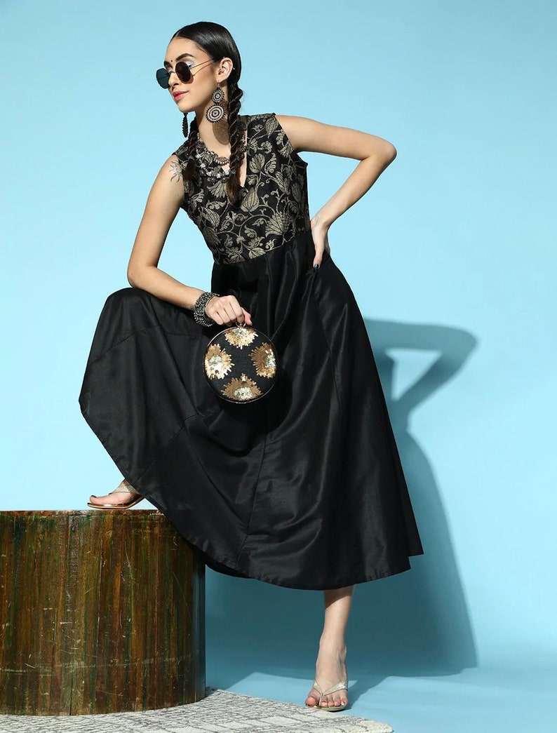 May include: A black sleeveless dress with a gold floral pattern on the bodice. The dress has a flowing skirt and is paired with black sunglasses, gold earrings, and a round gold and black clutch.