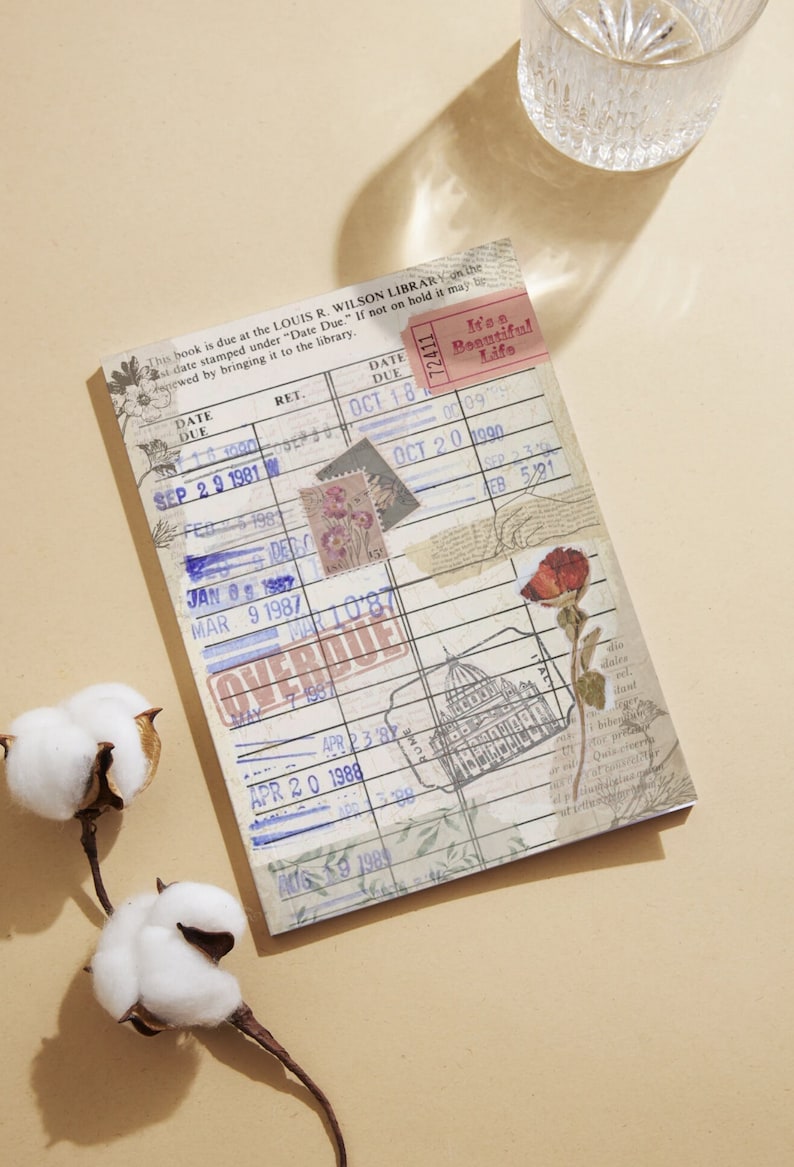 May include: A vintage library card with a blue and white design. The card has a date due stamp that says "Overdue" and a sticker that says "It's a Beautiful Life".