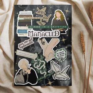 K&ouml;nnte beinhalten: Ein Satz Aufkleber mit Illustrationen einer Schlange, einer Hand, die eine andere Hand h&auml;lt, einer Person mit einem Vogel, einem gefalteten Papierkranich und einem Stapel B&uuml;cher. Die Aufkleber haben Text, der "Manacled", "A Rose in a Graveyard", "You are not replaceable", "Mudblood", "I'm tired of not getting to choose you", "Be careful", "Don't die", "I will allow a curse for you", und "Only because you asked" lautet.
