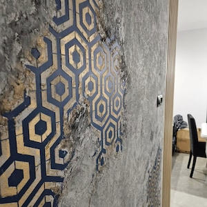 May include: A close-up of a textured grey wall with a geometric pattern in gold and navy blue. The design features a repeating honeycomb shape. The wall has a distressed appearance, with a wooden panel on the right.