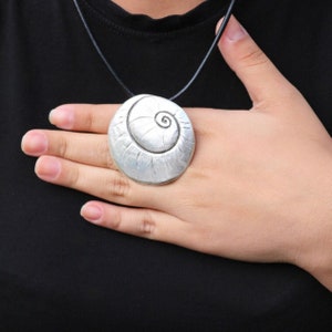 Könnte beinhalten: Eine silberne Halskette mit einem Anhänger in Form einer spiralförmigen Muschel. Der Anhänger ist rund und hat eine strukturierte Oberfläche.