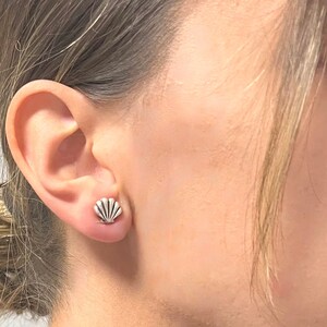 Könnte beinhalten: Nahaufnahme eines Ohrs mit einem kleinen silbernen Muschel-Ohrstecker.