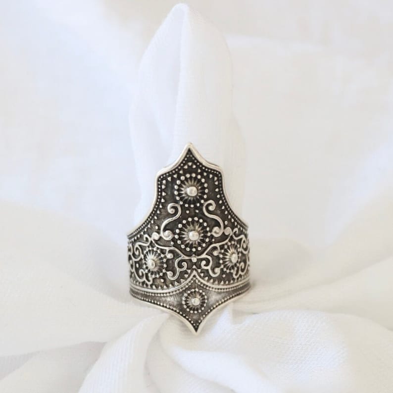 May include: A silver ring with an intricate, ornate design. The ring is shaped like a crown with a pointed top and a wide band.