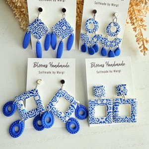 Puede incluir: Cuatro pares de pendientes hechos a mano con varios diseños geométricos. Los pendientes presentan un patrón azul y blanco y se exhiben en tarjetas blancas con el texto "Blooms Handmade Selfmade by Margi".