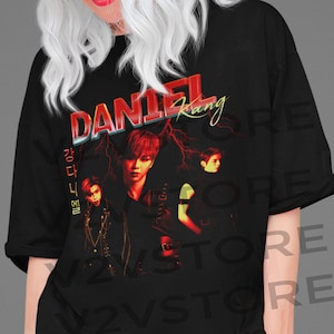 Könnte beinhalten: Schwarzes T-Shirt mit einem roten und weißen Grafikdruck eines koreanischen Popstars, Daniel Kang, mit dem Text "DANIEL Kang" in roten und weißen Buchstaben.
