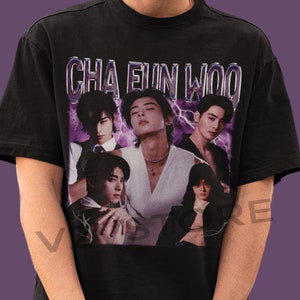 Pode incluir: Camiseta preta com uma estampa gráfica de um grupo de homens. A estampa apresenta o texto "CHA EUN WOO" em uma fonte prateada brilhante.
