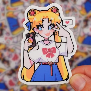 May include: A sticker featuring an anime-style character with blonde hair, blue eyes, and a white t-shirt with a pink bow. The character is holding a phone with an Instagram logo and making a peace sign.