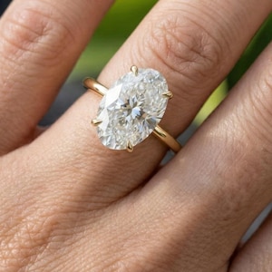 Anillo de compromiso ovalado de moissanita en oro amarillo de 14 quilates, solitario con halo oculto y puente de diamantes.