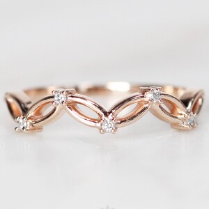 Puede incluir: Una delicada banda de anillo de oro rosa con un diseño ondulado con pequeños diamantes engastados en el metal.