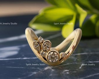 May include: A gold-colored ring with a curved design, featuring a cluster of round and marquise-cut diamonds. The ring is set against a dark, textured surface with the text "Spark Jewelry Studio".