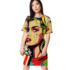May include: A yellow, red, blue, and black pop art style t-shirt dress featuring a woman with blonde hair and a large red mouth. The woman is holding a bucket of popcorn.