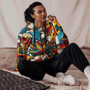 Puede incluir: Una sudadera con capucha negra con un estampado de c&oacute;mic colorido en amarillo, rojo, azul y blanco. El estampado incluye las palabras "BOOM" y "ZA".