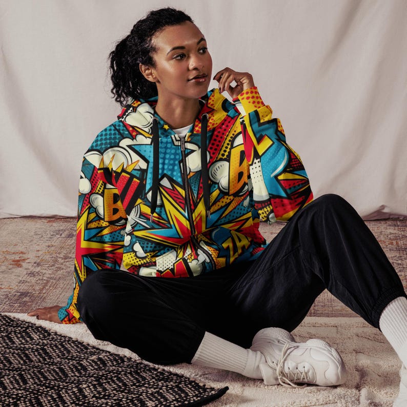 Puede incluir: Una sudadera con capucha negra con un estampado de c&oacute;mic colorido en amarillo, rojo, azul y blanco. El estampado incluye las palabras "BOOM" y "ZA".