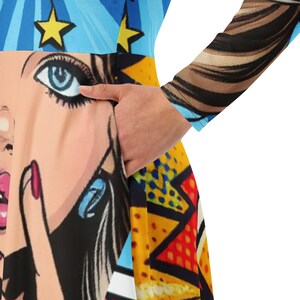 May include: A colorful dress featuring a pop art comic book style design. The dress has a vibrant pattern with a woman's face, stars, and geometric shapes in blue, yellow, and red. The long sleeve has a brown and black pattern.