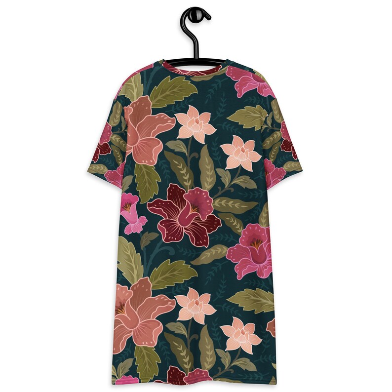 May include: A dark green t-shirt with a floral print featuring pink, red, and white flowers. The flowers are arranged in a repeating pattern on a dark green background.