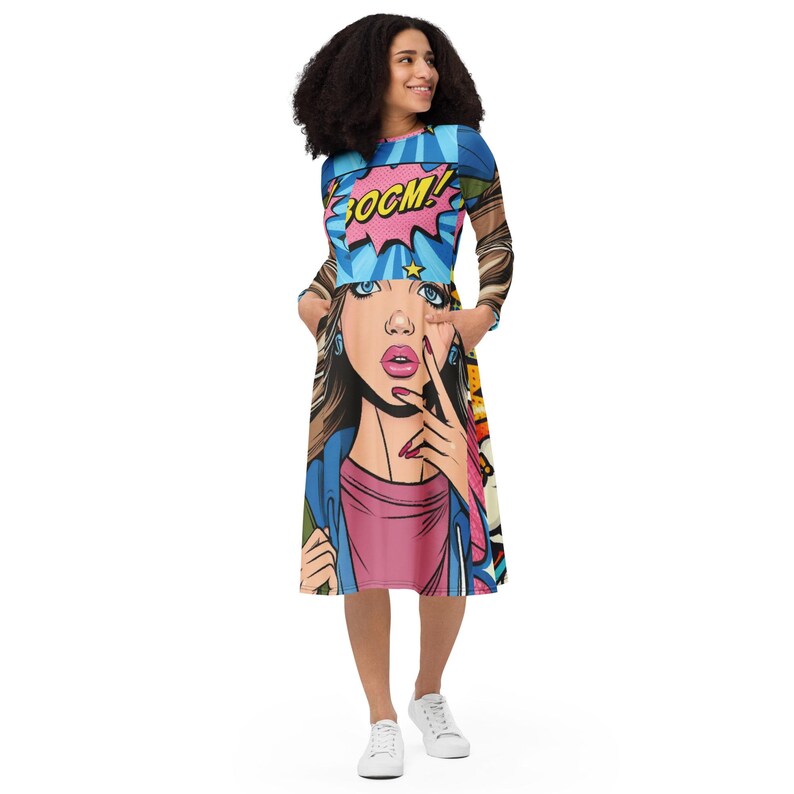 May include: A long-sleeved midi dress featuring a pop art comic book design. The dress showcases a vibrant illustration of a woman with the word "BOOM!" in a speech bubble. The dress has pockets and is made of a soft, comfortable material.
