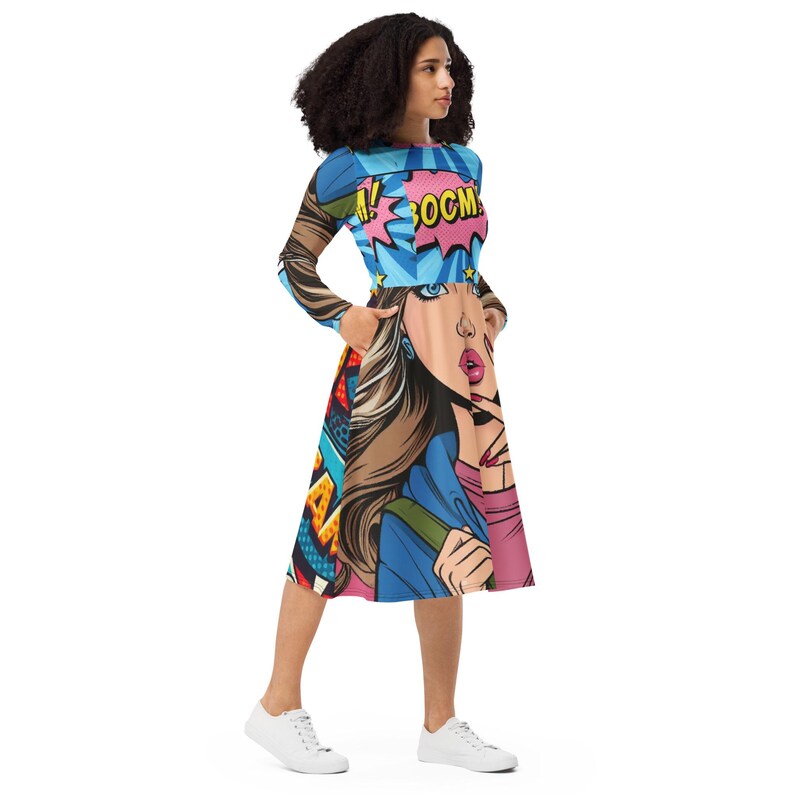 May include: A long-sleeved dress featuring a vibrant comic book-style illustration. The design includes a woman's face, speech bubbles with the word "BOOM", and colorful geometric patterns. The dress has a fitted bodice and a flared skirt.