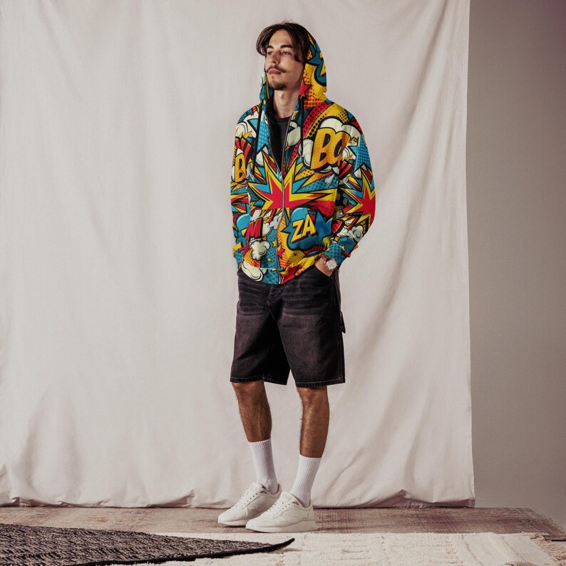 Puede incluir: Una chaqueta con capucha y cremallera con un estampado de c&oacute;mic colorido que incluye palabras como "BOOM" y "ZA". La chaqueta se lleva sobre una camiseta negra y pantalones cortos negros.