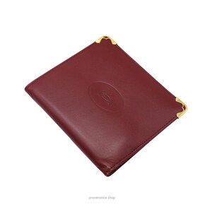May include: A red leather wallet with gold corners and a gold embossed Cartier logo.