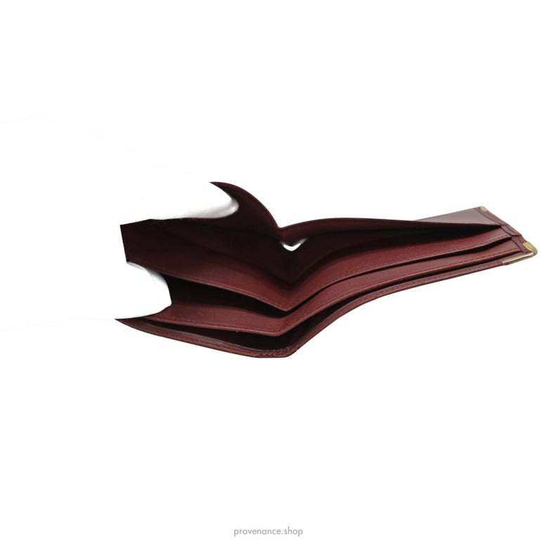 May include: A burgundy leather wallet folded open, showing the interior lining. The wallet has a smooth, textured surface and is made of high-quality leather.