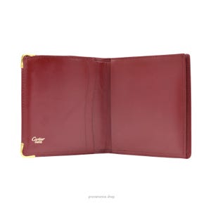 May include: Open red leather Cartier wallet with gold hardware and the words 'Cartier Paris' embossed on the front.