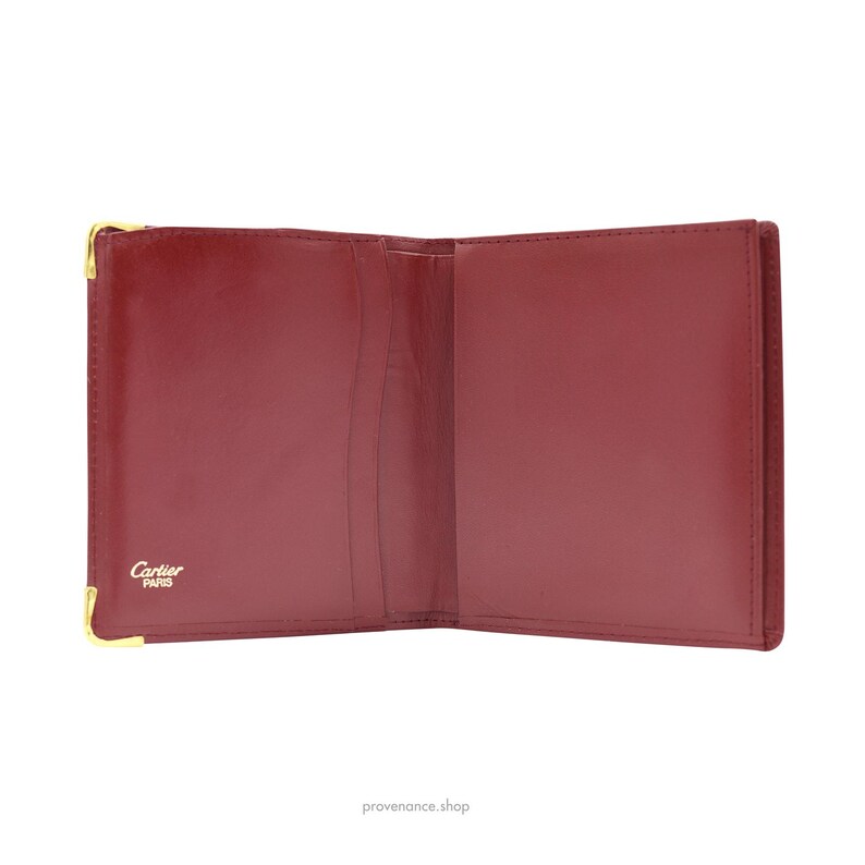 May include: Open red leather Cartier wallet with gold hardware and the words 'Cartier Paris' embossed on the front.
