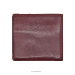 May include: A burgundy leather wallet with a smooth surface and a subtle sheen. The wallet is closed and has a simple design.
