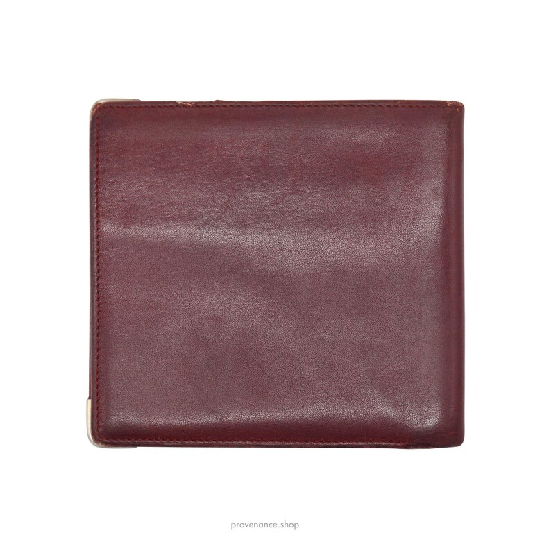 May include: A burgundy leather wallet with a smooth surface and a subtle sheen. The wallet is closed and has a simple design.