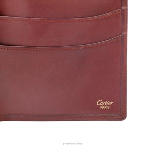 May include: A burgundy leather wallet with the words 'Cartier Paris' embossed in gold lettering.