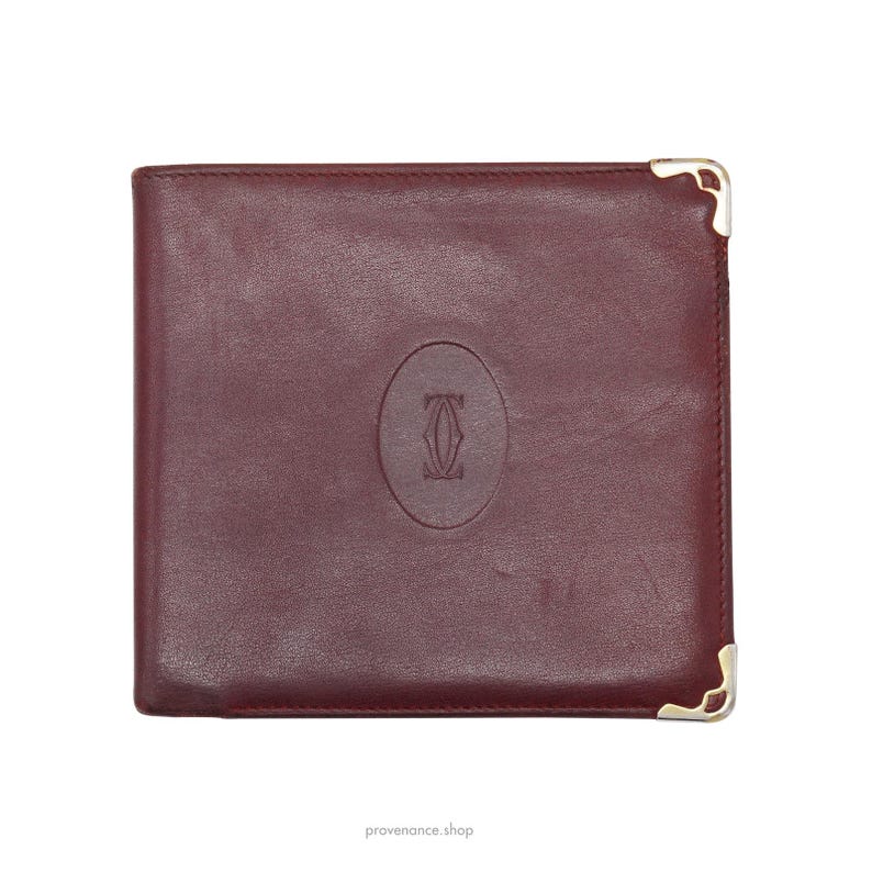 May include: A burgundy leather wallet with gold accents and a Cartier logo embossed on the front.