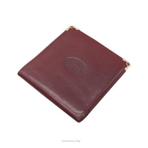 May include: A burgundy leather wallet with gold corners and a gold embossed Cartier logo.