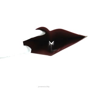 May include: The inside of a burgundy leather wallet is open and empty. The wallet is folded in half and the inside is visible.