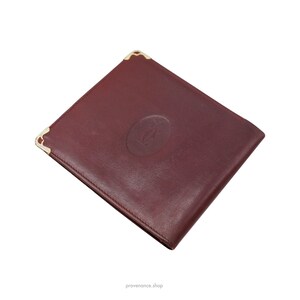 May include: A burgundy leather wallet with gold accents and a raised Cartier logo.