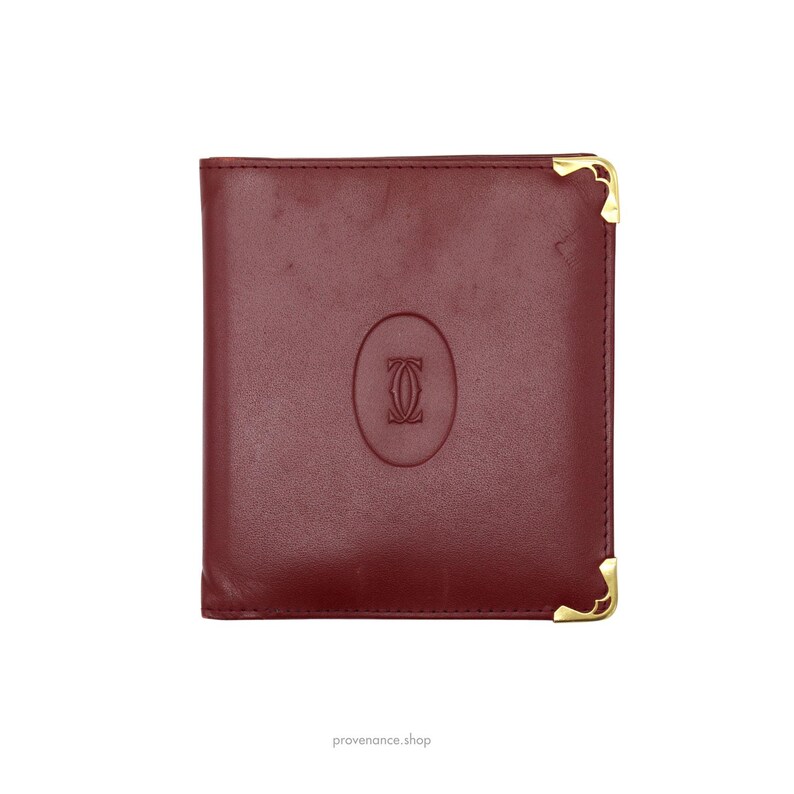 May include: A burgundy leather wallet with gold accents and a Cartier logo embossed on the front.