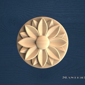 May include: A circular light-colored wooden medallion featuring a carved floral design with multiple pointed petals radiating from a central circular core. The wood grain is visible across the surface of the flower-shaped decorative element.