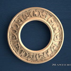 May include: A circular light-colored wooden frame featuring intricate carved scrollwork and leaf patterns along its border. The design includes symmetrical floral motifs and small circular accents. The text MASTERBUK is visible in the bottom right corner.