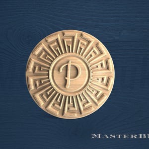 May include: A circular wooden carving with a sunburst design and the letter "P" in the center. The carving is light brown and set against a dark blue wooden background. The text "MASTERBUK" is at the bottom.