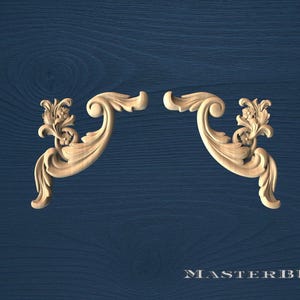May include: Two symmetrical, light-colored wooden decorative carvings with floral and scroll designs. The carvings are set against a dark blue wood-grain background. The text "MASTERBUK" is at the bottom.