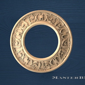 May include: A detailed, circular wooden carving with an ornate, floral design. The carving is light brown and features a central circular opening. The background is a dark blue wood grain. The text "MASTERBUK" is at the bottom.