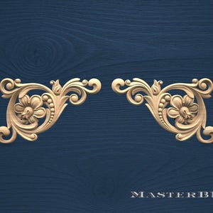 May include: Two symmetrical, light-colored wooden corner ornaments with floral and scroll designs. Each features a central flower surrounded by detailed carvings and a curved, ornate shape. The background is a dark blue wood grain.