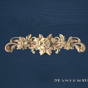 May include: A carved wooden floral embellishment featuring a central rose surrounded by leaves and smaller flower clusters. The design is symmetrical and detailed, with scrolling accents. The background is a dark blue wood grain. The text "MASTERBUK" is at the bottom.