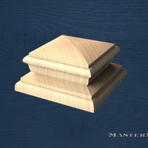 Op de afbeelding: Twee onafgewerkte houten paalkappen, op elkaar gestapeld. De kappen zijn vierkant met een afgeschuinde bovenkant en een decoratieve rand. Het hout heeft een lichte, natuurlijke kleur. Waarschijnlijk voor een hek of terras.