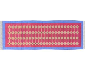 Puede incluir: Una alfombra de pasillo roja y azul con un patrón geométrico de cuadrados beige y círculos verdes. La alfombra tiene flecos en los extremos.