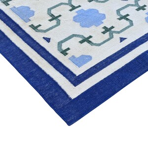 May include: A white rug with a blue and green geometric pattern. The rug has a blue border.