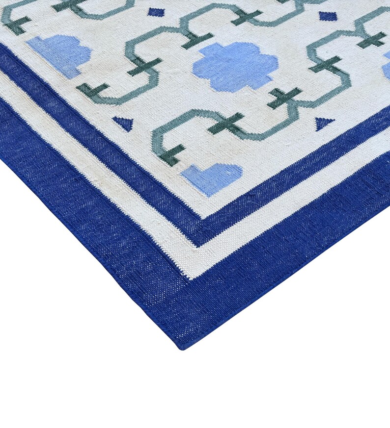 May include: A white rug with a blue and green geometric pattern. The rug has a blue border.